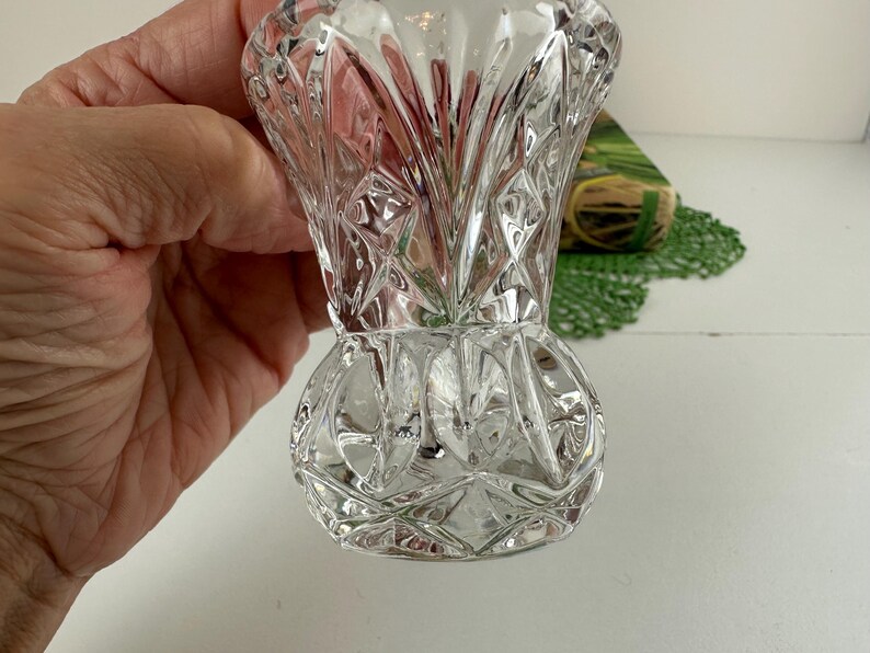 K&ouml;nnte beinhalten: Eine klare Glasvase mit einem facettierten Diamantschliffmuster auf der Oberfl&auml;che. Die Vase hat einen ausgestellten Rand, einen schmalen Hals und einen abgerundeten, bauchigen Fu&szlig;. Das Glas ist transparent und bricht das Licht.