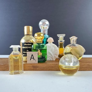 May include: A collection of vintage perfume bottles in various shapes and sizes. The bottles are made of glass and feature different colored liquids. One bottle has a gold cap and the text "Parfum Rendez-Vous". Another bottle has a green liquid and a gold horse logo.