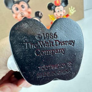 May include: Close-up of the bottom of a vintage Mickey Mouse figurine. The black base is heart-shaped and features the text "&copy; 1986 The Walt Disney Company" and "TOOTSIETOY&reg; MADE IN CHINA."