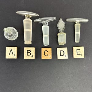 May include: Five glass bottle stoppers with different shapes and sizes. The stoppers are labeled A, B, C, D, and E.