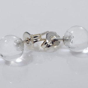 Puede incluir: Un par de pendientes de plata con esferas de cristal transparente. Los pendientes son simples y elegantes.