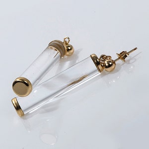 May include: A pair of gold tone earrings with clear glass tubes. The tubes are hollow and have a gold tone cap on one end. The earrings have a post back.