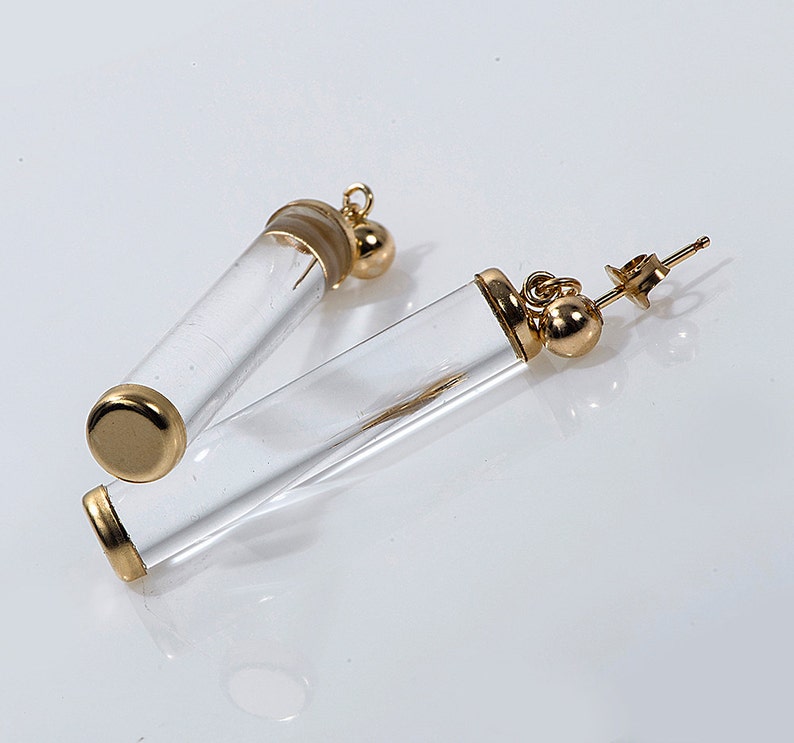 May include: A pair of gold tone earrings with clear glass tubes. The tubes are hollow and have a gold tone cap on one end. The earrings have a post back.