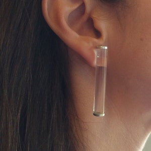 May include: A pair of clear acrylic long bar earrings. The earrings are approximately 5 cm long and have a silver metal backing.