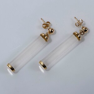 May include: A pair of gold earrings with white cylindrical stones. The stones are translucent and have a smooth finish.