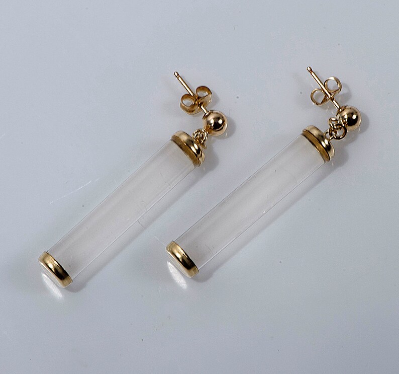 May include: A pair of gold earrings with white cylindrical stones. The stones are translucent and have a smooth finish.