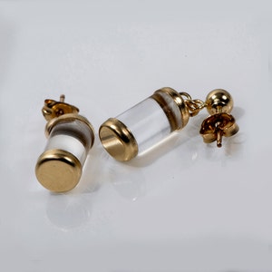 May include: A pair of gold earrings with clear glass cylinders. The cylinders have a gold band around the top and bottom.