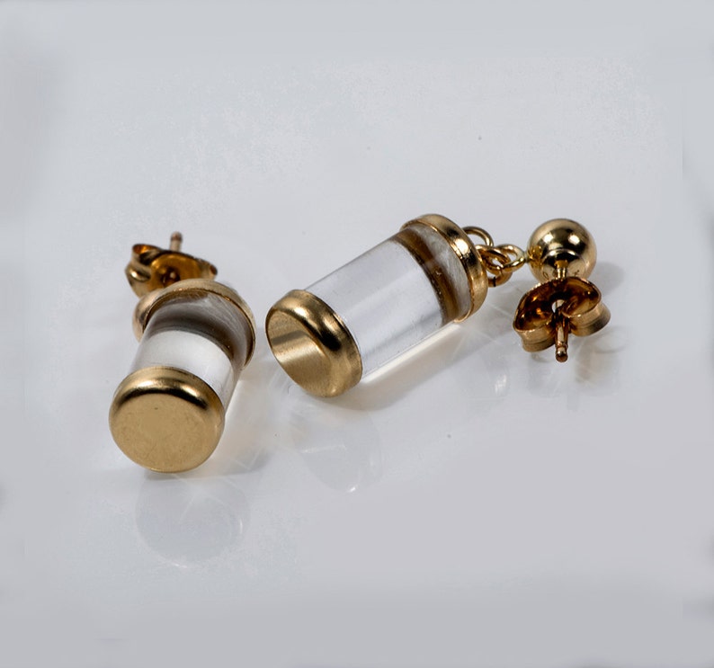 May include: A pair of gold earrings with clear glass cylinders. The cylinders have a gold band around the top and bottom.
