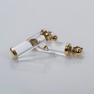 May include: A pair of gold and clear crystal earrings. The earrings are shaped like small tubes with a gold ball at the bottom.