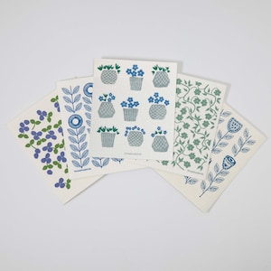 May include: A collection of five white, absorbent cleaning cloths with various blue and green floral designs. The cloths feature patterns of flowers, leaves, and stylized flower pots. The cloths are arranged in a fan shape against a white background.