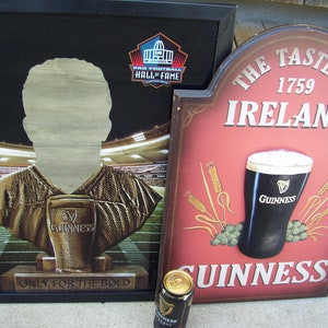 May include: A red and white sign with the text "The Taste of Ireland 1759" and a depiction of a pint of Guinness beer. The sign is made of wood and has a distressed look.