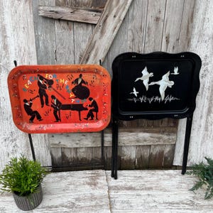 May include: Two rectangular metal TV tray tables with folding black legs. The left tray is orange with black silhouettes of a jazz band and the text "REACH FOR THE RHYTHM". The right tray is black with white silhouettes of flying ducks.