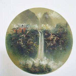 Pu&ograve; includere: Un dipinto di una cascata che scende a cascata da un fianco di una montagna, con un piccolo edificio rosso e una lussureggiante vegetazione verde in primo piano. Il dipinto &egrave; di forma circolare, conferendogli un aspetto unico e artistico.