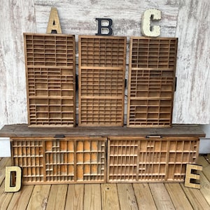 May include: Five rectangular wooden printer trays with multiple small compartments arranged in a grid pattern. Three trays are positioned vertically with letters A, B, and C above them, and two trays are positioned horizontally with letters D and E.