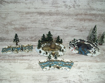 May include: Four miniature winter village scenes with snow-covered trees, a small bridge, and a frozen river. The scenes are made of painted plaster and are designed to be used as decorations.