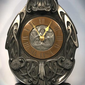 May include: A silver Celtic knot clock with a copper face and gold hands. The clock is in the shape of a stylised Celtic knot and has a three-dimensional design.