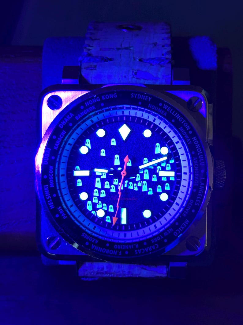 May include: A square-faced wristwatch with a dark blue face and a light blue glow. The watch face displays city names and small, white, glowing shapes. The watch has a brown leather band and a metal case.