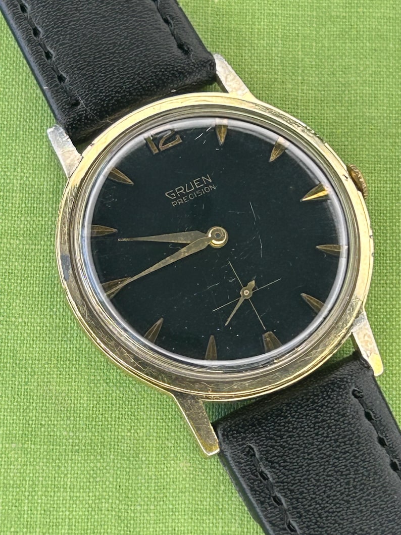 Vintage 1960s Gruen Precision watch.  Black leather band.  Running, serviced, keeps time, working.  Gold plated case with black dial