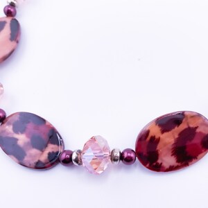 Könnte beinhalten: Eine Halskette mit Leopardenmuster in Rosa und Braun mit klaren Kristallperlen und dunkelvioletten Perlen.