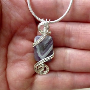 May include: A silver chain necklace with a pendant featuring a purple and white striped stone wrapped in silver wire.
