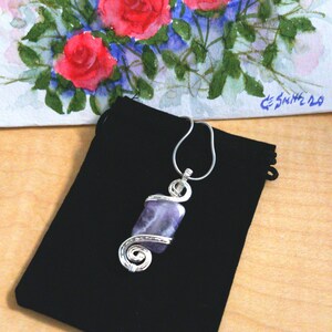 May include: A silver wire wrapped pendant featuring a purple amethyst stone. The pendant is displayed on a black velvet pouch.