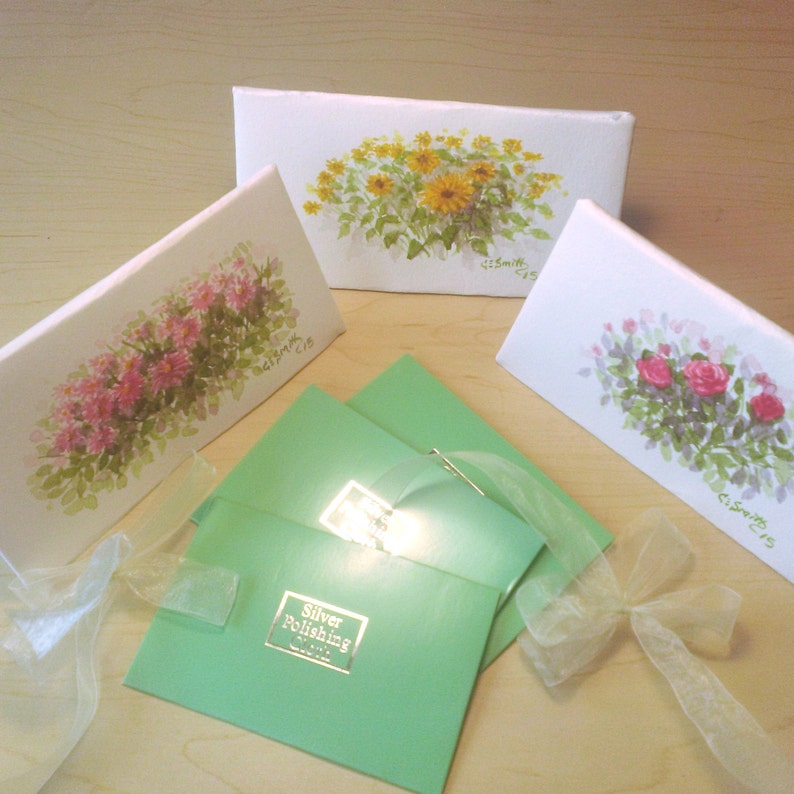 May include: Three white cards with floral paintings and the text "C. Smith '15" on each. A green envelope with the text "Silver Polishing Cloth" is in the center of the image.