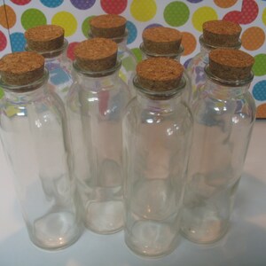 May include: Eight clear glass bottles with cork tops. The bottles are all the same size and shape, and they are arranged in a row.