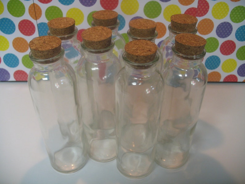 May include: Eight clear glass bottles with cork tops. The bottles are all the same size and shape, and they are arranged in a row.