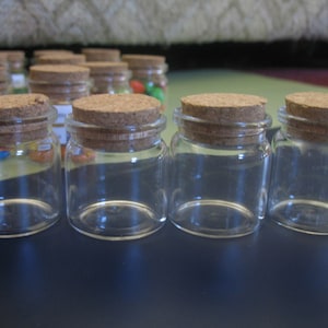 May include: Four clear glass jars with cork lids. The jars are empty and have a round shape.