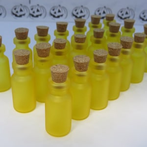May include: A group of 20 small, yellow glass bottles with cork stoppers. The bottles are arranged in a triangular shape.