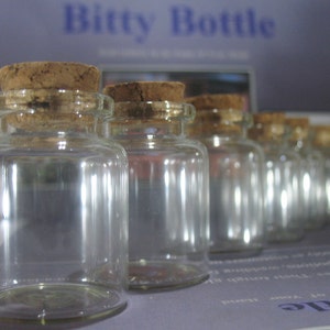 May include: A row of small, clear glass bottles with cork tops. The bottles are arranged in a line, with the largest bottle in the front and the smallest bottle in the back. The bottles are all empty and have a slightly textured surface.