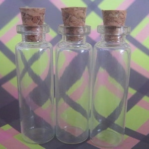 May include: Three clear glass bottles with cork stoppers. The bottles are empty and have a cylindrical shape.