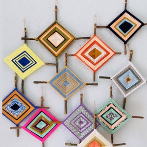 May include: A collection of 10 colorful dreamcatchers, each with a unique pattern and color scheme, are hung on a white wall. The dreamcatchers are made with yarn and are attached to sticks.