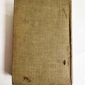 May include: A vintage book with a textured, olive-green cover. The cover shows signs of wear, including stains and discoloration. The spine is a darker shade of brown. The book is rectangular and appears to be closed.