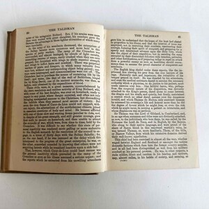 May include: An open vintage book with aged, yellowed pages. The text on the pages is in English, with the title "THE TALISMAN" visible at the top of the page. The book's spine is visible.