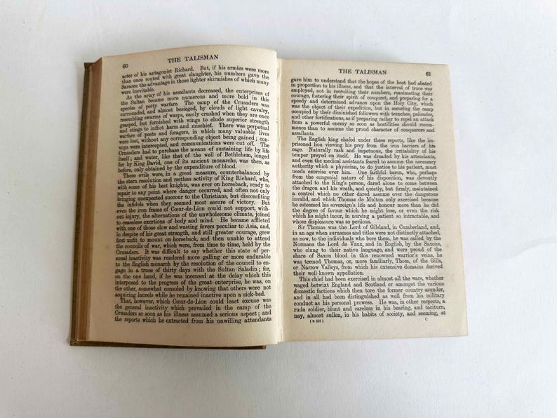 May include: An open vintage book with aged, yellowed pages. The text on the pages is in English, with the title "THE TALISMAN" visible at the top of the page. The book's spine is visible.