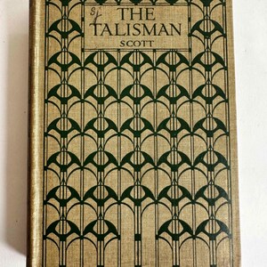 May include: A vintage book titled "The Talisman" by Scott. The cover features a tan background with a repeating dark green geometric pattern. The title and author's name are in dark green, with the title in a stylized font.