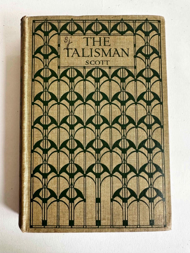 May include: A vintage book titled "The Talisman" by Scott. The cover features a tan background with a repeating dark green geometric pattern. The title and author's name are in dark green, with the title in a stylized font.