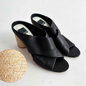 May include: Black leather slip-on sandals with a crisscross design. The sandals have a rounded toe and a stacked heel with a woven texture. The heel height appears to be approximately 3 inches.