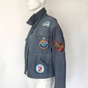 K&ouml;nnte beinhalten: Eine blaue Jeansjacke mit verschiedenen Patches, darunter ein Schmetterling, eine Blume und ein Logo mit der Aufschrift "Lee Tires".