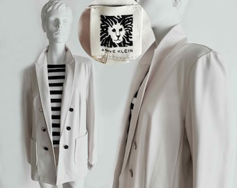 Puede incluir: Un blazer beige claro con botones negros y bolsillos delanteros. El blazer cruzado se lleva sobre una camiseta a rayas blancas y negras. La etiqueta Anne Klein es visible en la esquina superior derecha.