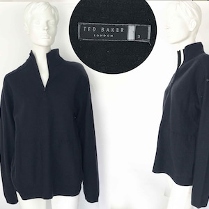 May include: A black long-sleeved sweater with a zipper and a high collar. The sweater has a Ted Baker London label on the sleeve.