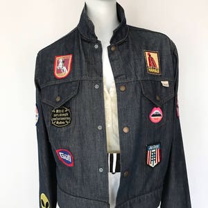 Peut inclure: Une veste en jean bleu fonc&eacute; avec une vari&eacute;t&eacute; de patchs, dont un patch rouge, blanc et bleu avec le texte "With all our strength and courage we confront tomorrow My Dreams", un patch rouge, blanc et bleu avec le texte "Join Corps", un patch rouge, blanc et bleu avec le texte "Goll", un patch rouge, blanc et bleu avec le texte "Hawaii", un patch rouge, blanc et bleu avec un cheval et un cavalier, et un patch rose avec une paire de l&egrave;vres.