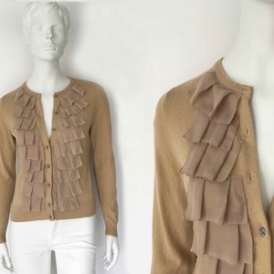 May include: A beige cardigan with a ruffled trim. The cardigan has a button closure and long sleeves.
