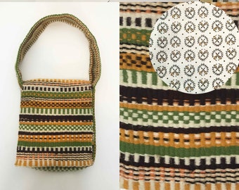 May include: A small, green, brown, and white woven bag with a strap. The bag has a geometric pattern and is made of a thick, textured fabric.