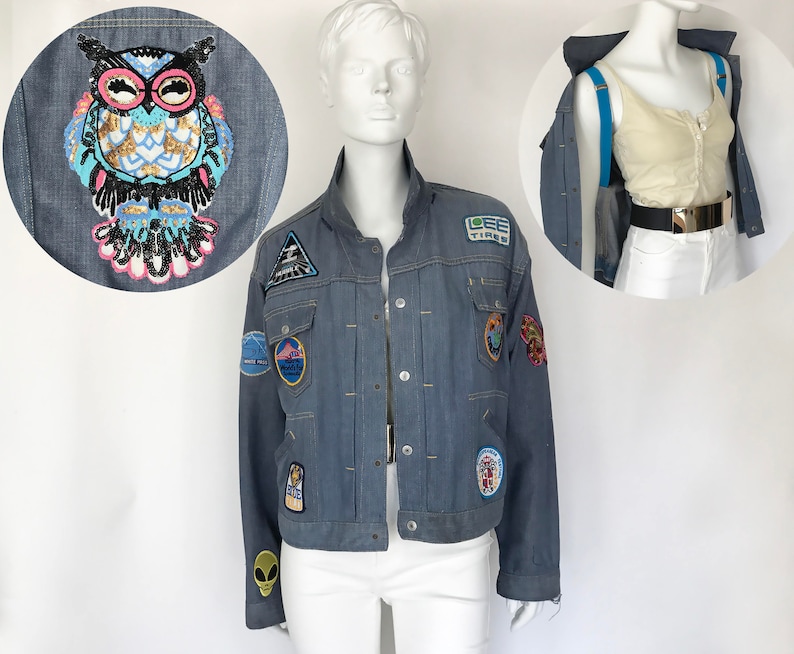 K&ouml;nnte beinhalten: Eine blaue Jeansjacke mit verschiedenen bunten Patches, darunter ein Eulen-, ein Dreiecks- und ein Globus-Patch. Die Jacke hat einen Rei&szlig;verschluss und zwei Fronttaschen.