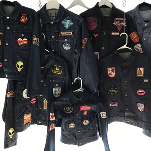 K&ouml;nnte beinhalten: Eine Sammlung von zehn Jeansjacken mit verschiedenen Patches und Designs. Die Jacken sind alle in verschiedenen Farben und Stilen gehalten, einige haben gestickte Patches, w&auml;hrend andere B&uuml;gelbilder haben. Die Jacken sind alle in gutem Zustand und w&auml;ren eine gro&szlig;artige Erg&auml;nzung f&uuml;r jede Garderobe.