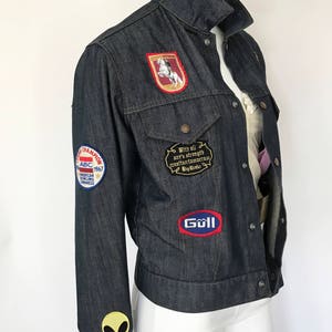 Peut inclure: Une veste en jean bleu fonc&eacute; avec divers patchs, dont un cheval et un cavalier, un ovale rouge et bleu avec le mot "Goll" et un patch blanc avec le texte "With all our strength creation tomorrow Big Dreams". La veste a &eacute;galement un patch d'alien vert sur la manche gauche et un patch rouge, blanc et bleu avec le texte "ABC 1967 American Bowling Congress".