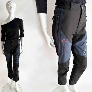 May include: Black and blue outdoor trousers with a mountain logo. The trousers have multiple pockets and zips. The trousers are displayed on a mannequin.