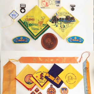 Op de afbeelding: Een verzameling scouting-souvenirs, waaronder badges, neckerchiefs en linten. De items bevatten verschillende ontwerpen, waaronder een hert, een kampscene en een brug. De badges zijn uit verschillende jaren en locaties, waaronder de National Jamboree van 1969 in Idaho en het Kaufman Scout Camp in New York.